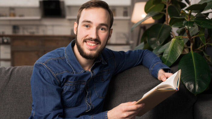 Professional Headshot of a writer wearing denim shirt at home & sitting on the sofa, captured in a cozy setting. 