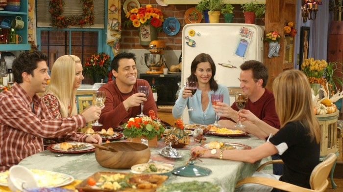 A photo of the cast of the Friends show celebrating Thanksgiving around a food table. 