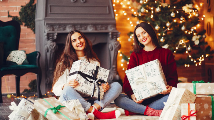  A photo of two friends around surrounded by Christmas presents and a Christmas tree in an indoor setting.