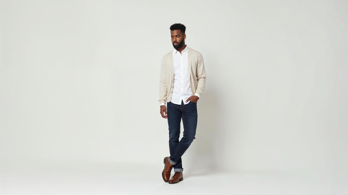 A photo of a man in a classic white button-up shirt with a cardigan, dark jeans, neutral chinos, and derby shoes.